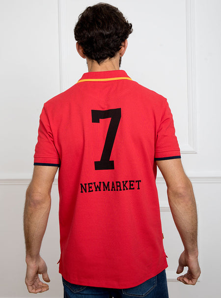 Man wearing red polo shirt in 100% cotton with Newmarket 875 crest embroidered on the front with navy sleeve trimming and gold collar trimming.